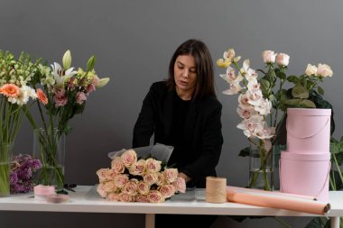 Çiçek buketini sıraya dizen bir çiçekçi. Çiçekçinin masasında gül çiçeklerini kağıda sarmak.
