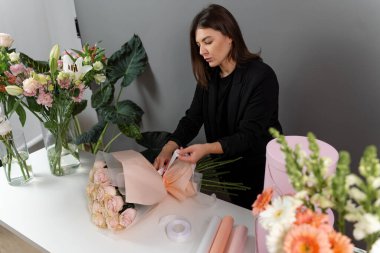 Teslimat için güllerden taze buket yapıyorum. Çiçekçi çiçekçi dükkanındaki siparişe bir çiçek aranjmanı bağlıyor.