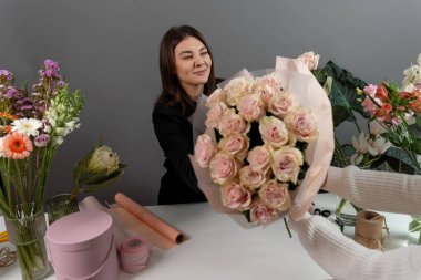 Teslimat için çiçek aranjmanı. Çiçekçi, gri duvar arkaplanındaki kuryeye taze çiçek veren pastel pembe güller verir.