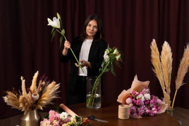 Çiçekçi teslimat için çiçeklerden bir kompozisyon yapar. Tatil için zambak buketi. Kadınlar çiçekçide zambak buketi toplarlar.