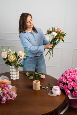 Beste yapmadan önce taze çiçekler hazırlıyorum. Kadın çiçekçi elinde bir buket kompozisyon tutuyor ve dizayn ediyor. Stüdyoda çiçek buketi yapan çiçekçi.