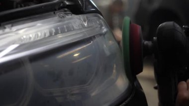 Hands with orbital polisher, polishing black car in detailing center to restore cloudy headlight 4k video. Hard wax car headlight polishing with orbital polisher for remove scratches.