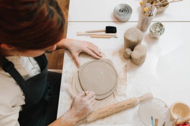 Genç çömlekçi atölyede çömlekçilikle bir çember keser. Kil modelleme için hazırlanılıyor, kapatılıyor