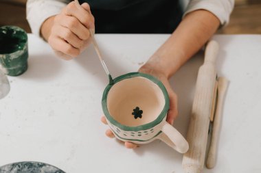 Sanatçı, fırın yangınından sonra kil seramik bardakta süsleme yapıyor. Geleneksel desenli toprak kapları tasarla