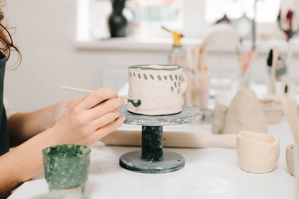 Художник украшает и рисует вручную керамические чашки глины в творческой мастерской. Художник рисует и добавляет уникальные конструкции в глиняную посуду