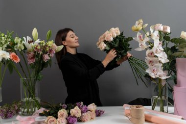 Özel sipariş için çiçek bileşimi topluyorum. Gri arka plan çiçek stüdyosunda çiçekçinin pembe güllerinden buket hazırlıyorum.