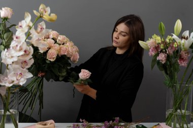 Gri arka plan çiçek stüdyosundaki çiçekçinin pembe güllerinden buket yapıyorum. Özel sipariş için çiçek bileşimi toplanıyor