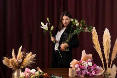 Çiçekçi teslimat için çiçeklerden bir kompozisyon yapar. Tatil için zambak buketi. Kadınlar çiçekçide zambak buketi toplarlar.