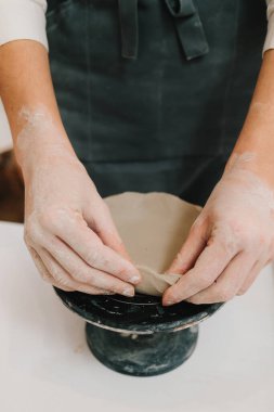 El sanatları stüdyosundaki balçığı tabağa dönüştüren eller. Sanatçı seramik kaseyi çömlekçi tekerleği kullanarak yontuyor.