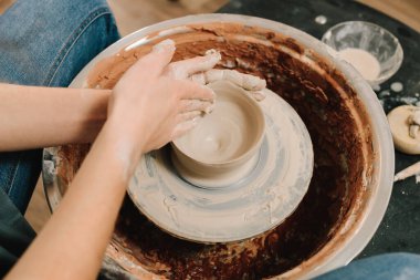 Zanaatkar dönen tekerleğin üzerinde bir çömlek tabağı yontuyor. Sanatçı kadın çömlek atölyesinde porselen kaplar yapıyor.