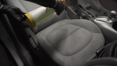 4K kuru temizleme videosu için tekstil koltuklarına deterjan sıkıyorum. Profesyonel eldiven temizleyicisi arabada koltuğa leke ve kir çıkarmak için deterjan döküyor..
