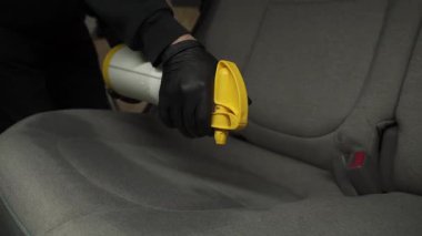 4K kuru temizleme videosu için tekstil koltuklarına deterjan sıkıyorum. Profesyonel eldiven temizleyicisi arabada koltuğa leke ve kir çıkarmak için deterjan döküyor..