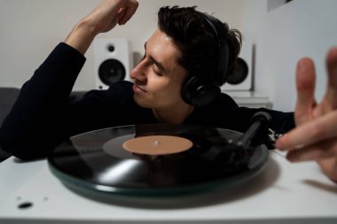 Duygusal müzik aşığı bir pikapta vinil plak dinliyor. Neşeli hipster vinil plaklardan müzik dinliyor ve müzik aşığının gerçek duygularını hissediyor.