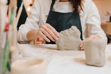 Potter seramik ürünleri için ıslak kil heykeli yapıyor. Çömlek atölyesindeki masaya seramik kil ürünü yapan bir kadın çömlekçinin elleri.