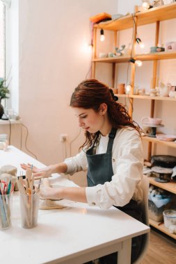 Zanaatkar kadın balçığı oklavayla kaplıyor, yakın plan. Kadın esnaf seramik stüdyosunda çömlek aletleriyle killeri dikkatlice sarar.