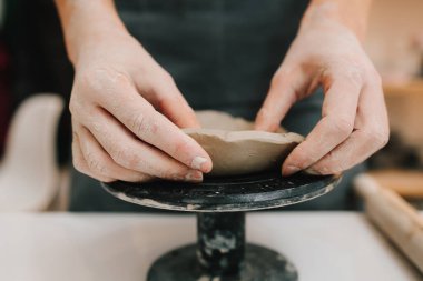 El sanatları stüdyosundaki balçığı tabağa dönüştüren eller. Sanatçı seramik kaseyi çömlekçi tekerleği kullanarak yontuyor.