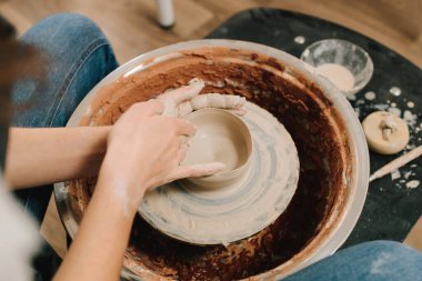 Zanaatkar dönen tekerleğin üzerinde bir çömlek tabağı yontuyor. Sanatçı kadın çömlek atölyesinde porselen kaplar yapıyor.