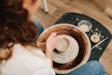 Zanaatkar dönen tekerleğin üzerinde bir çömlek tabağı yontuyor. Sanatçı kadın çömlek atölyesinde porselen kaplar yapıyor.