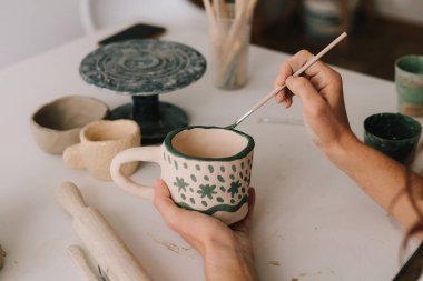 Geleneksel desenli bir toprak kap tasarla. Sanatçı, fırın ateşinden sonra kil seramik bardak üzerine dekorasyon yapıyor.