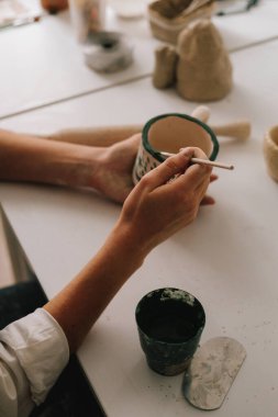 Deneyimli ressam çömlekçilik atölyesindeki seramik bardak üzerine tasarım yapıyor. Potter, soyut bir tasarımı toprak kabına çizer.