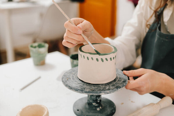 Художник рисует и добавляет уникальные конструкции в глиняную посуду. Художник украшает и рисует вручную керамические чашки глины в творческой мастерской