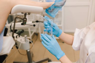 Jinekolog muayene koltuğunda hamile kadını muayene ediyor. Jinekolog klinikte bakteri muayenesi için vajinadan örnek alır.