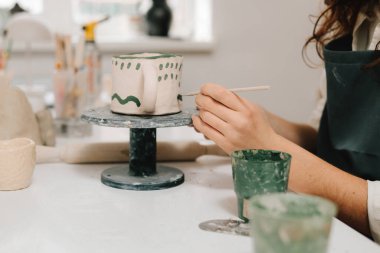 Ressam, toprak eşyasına eşsiz tasarımlar çiziyor ve ekliyor. Sanatçı yaratıcı atölyede el yapımı seramik kil bardak dekorasyonu ve boyama yapıyor.
