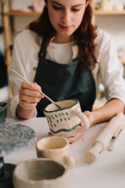 Deneyimli ressam çömlekçilik atölyesindeki seramik bardak üzerine tasarım yapıyor. Potter, soyut bir tasarımı toprak kabına çizer.