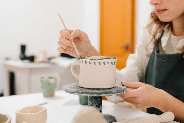 Художник рисует и добавляет уникальные конструкции в глиняную посуду. Художник украшает и рисует вручную керамические чашки глины в творческой мастерской