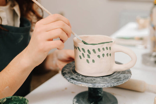 Художник рисует и добавляет уникальные конструкции в глиняную посуду. Художник украшает и рисует вручную керамические чашки глины в творческой мастерской