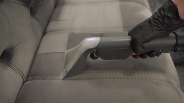 Temizlikçi, deterjan 4k video ile temizleme makinesi kullanarak kanepeyi temizliyor. Döşeme mobilyalarının tozunu ve lekelerini temizlemek için sökücü kullanıyor..