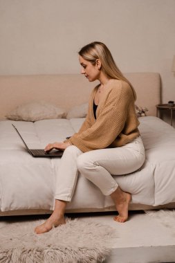 Bilgisayarlı kız evde çalışıyor. Genç kadın yatakta oturuyor ve dizüstü bilgisayarda yazıyor. Uzaktan kumanda. IT Uzmanı iş arkadaşlarıyla internette sohbet ediyor.