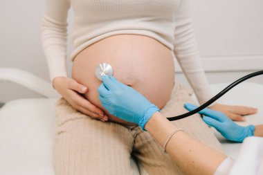 Hamilelik kontrolü. Jinekolog ve steteskoplu bir jinekolog jinekoloji kliniğindeki randevuda bebeğin kalp atışlarını dinliyor.