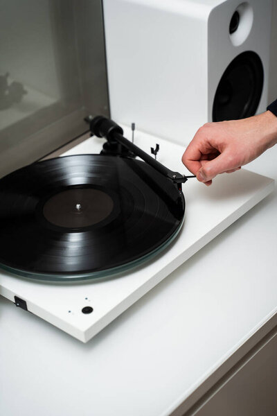 Music lover is holding tonearm in hand before playing the vinyl retro music on vinyl turntable. Musician adjusts tonearm on vinyl turntable