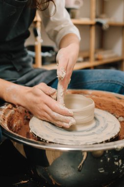 Sanatçı kadın çömlek atölyesinde porselen kaplar yapıyor. Zanaatkar dönen tekerleğin üzerinde bir çömlek tabağı yontuyor.