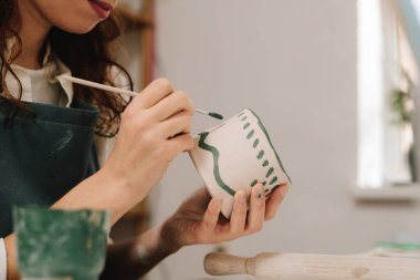 Ressam bir kil kabı çiziyor ve renkli bir dekorasyon yapıyor. Kadın sanatçı atölyede boya fırçası ve su renkleriyle toprak malzemesi boyuyor.