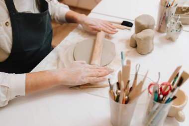 Kadın esnaf seramik stüdyosunda çömlek aletleriyle killeri dikkatlice sarar. İşçi çamuru merdaneyle biçimlendirir