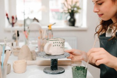 Sanatçı yaratıcı atölyede el yapımı seramik kil bardak süsleme ve boyama yapıyor. Ressam, toprak eşyasına eşsiz tasarımlar çiziyor ve ekliyor