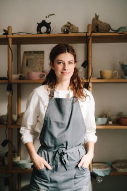 Onun çömlekçi stüdyosunun arka planında toprak eşyalarıyla dolu raflarla mutlu bir genç çömlekçi duruyor ve gülümsüyor. Küçük işletmeleri başarılı bir zanaatkar kadın yönetiyor.