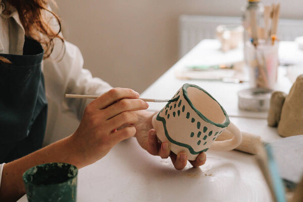 Поттер рисует абстрактный дизайн в глиняной чашке. Опытный художник рисует на керамической чашке в керамической мастерской