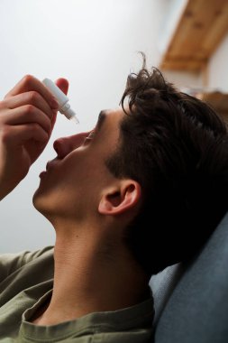 Genç adam tahriş sorunu için göz damlası kullanıyor. Adam evdeki göz sağlığından tıbbi göz damlası damlatıyor.