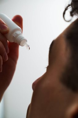 Evde göz damlası ile göz tedavisi uygulanıyor. Sinir bozukluğundan gözlerinden damlayan bir adam.