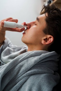Hasta hasta sinüzit tedavisi için burun damlası alıyor. Adam evde doktor reçetesiyle ilaç ve sprey kullanıyor.