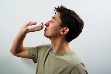 Hasta beyaz arka planda sinüzit tedavisi için burun damlası alıyor. Adam grip için burun spreyi kullanıyor.