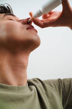 Hasta beyaz arka planda sinüzit tedavisi için burun damlası alıyor. Adam grip için burun spreyi kullanıyor.