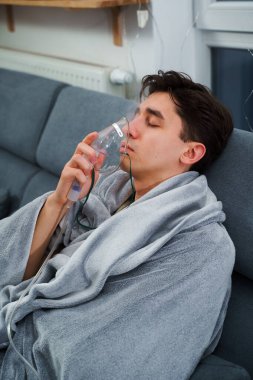 Evde öksürük tedavisi için nebulizör maskesiyle hava solumak. Hasta adam nebulizatörle solunum tedavisi görüyor.