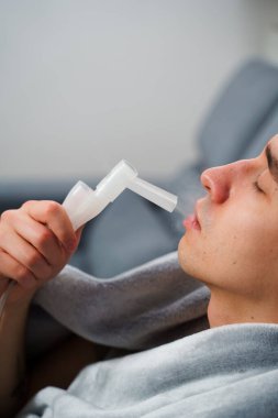 Evde nebulizatörün yardımıyla ağız solunumu. Hasta adam evde grip tedavisi için ağız spreyi nebulizatörü kullanıyor.