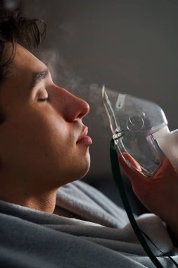 Öksürük tedavisi için oksijen maskesi yutan bir adam. Evde hastalık tedavisi için kompresör nebulizörü kullanılıyor.