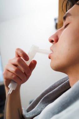 Evde nebulizatörün yardımıyla ağız solunumu. Hasta adam evde grip tedavisi için ağız spreyi nebulizatörü kullanıyor.