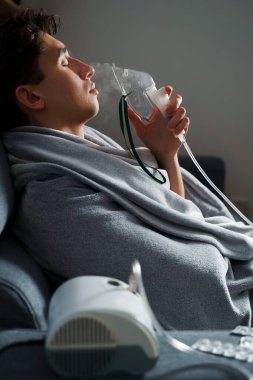 Öksürük tedavisi için oksijen maskesi yutan bir adam. Evde hastalık tedavisi için kompresör nebulizörü kullanılıyor.